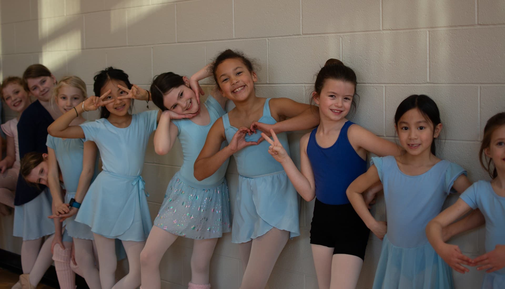 Art in Motion Dance ballet students in light blue leotards posing along a studio wall